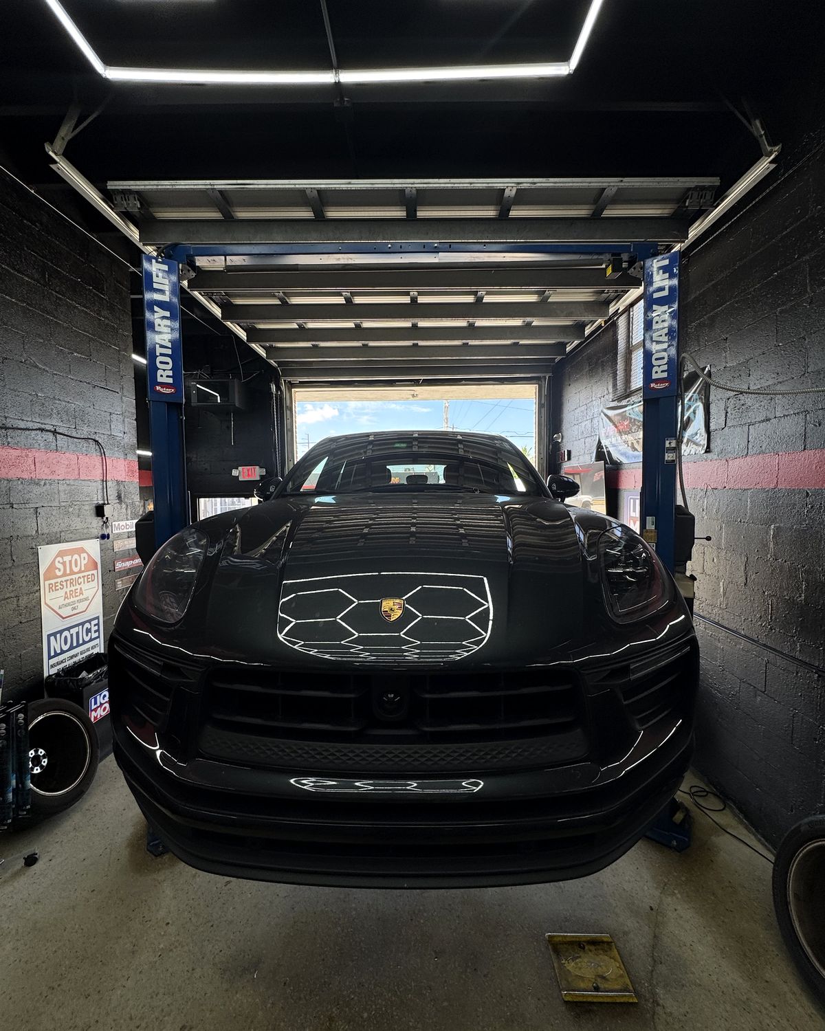 Black Porsche Macan on the lift, the hexagon ceiling lights reflected in its hood