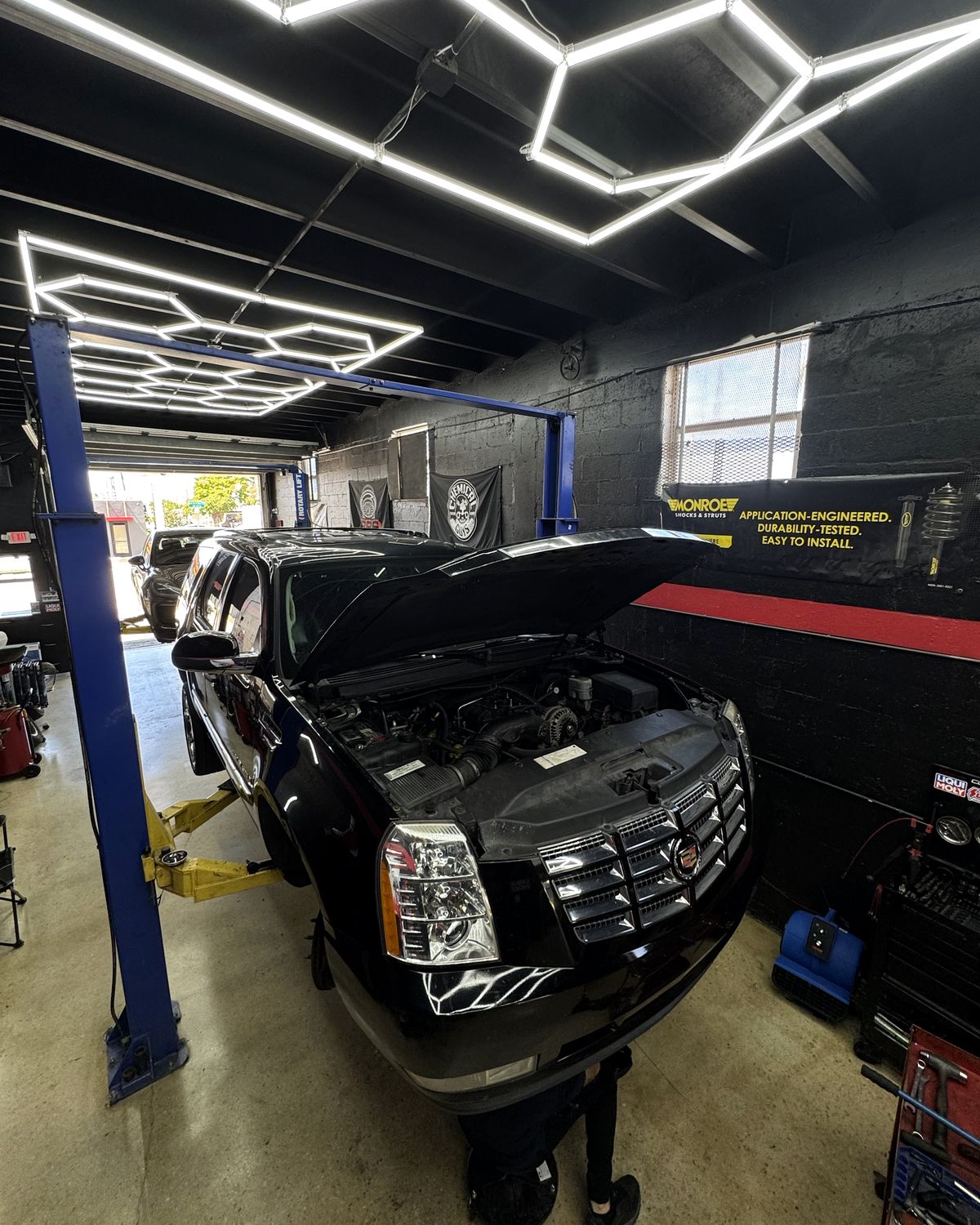 Black Cadillac Escalade with the hood open under the shop's hexagon ceiling lights